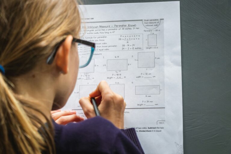 Student with glasses and blonde hair in ponytail writes on paper math test with rectangles.