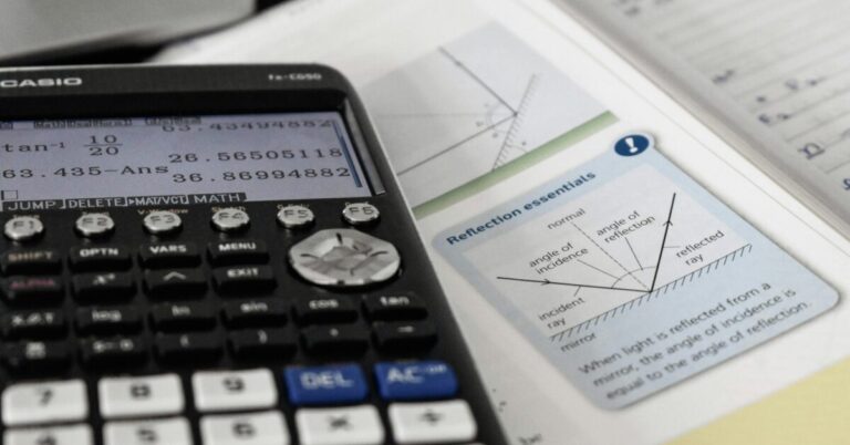 Calculator with trigonometric functions sitting on top of open mathematics text book.